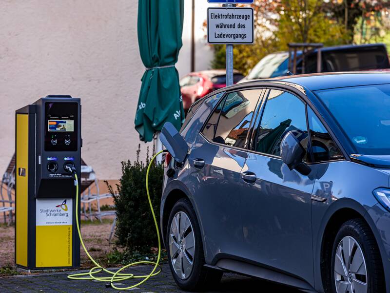 Eine gelb-graue E-Ladestation für Elektroautos. Von der Ladestation führt ein Ladekabel in die Tanköffnung eines grauen Autos.
