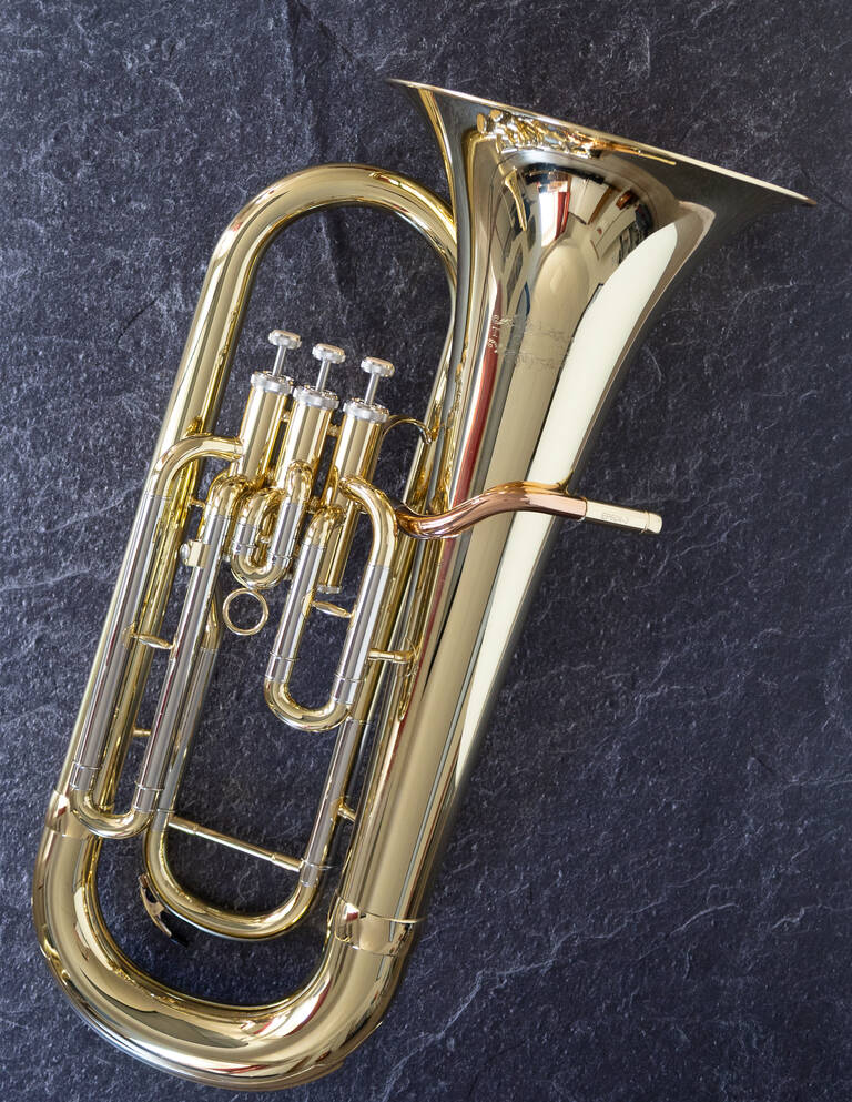 Auf dem Bild ist ein glänzendes, goldfarbenes Euphonium vor einem dunklen Hintergrund zu sehen.