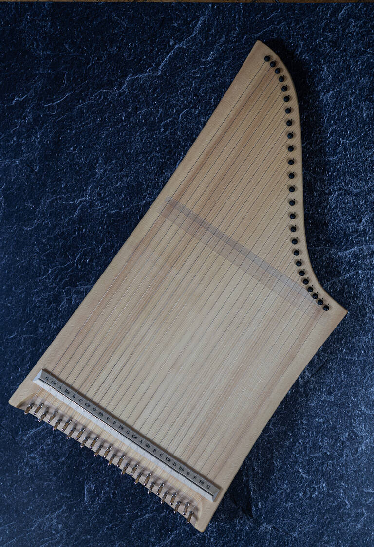 Das Bild zeigt eine Kastenzither, ein Musikinstrument mit zahlreichen Saiten, die auf einer hellen Holzdecke aufgespannt sind.